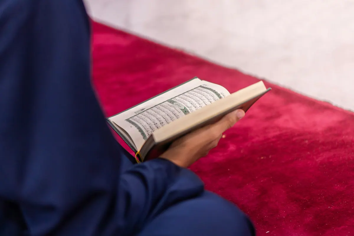 Woman reading the Quran on a mosque prayer carpet